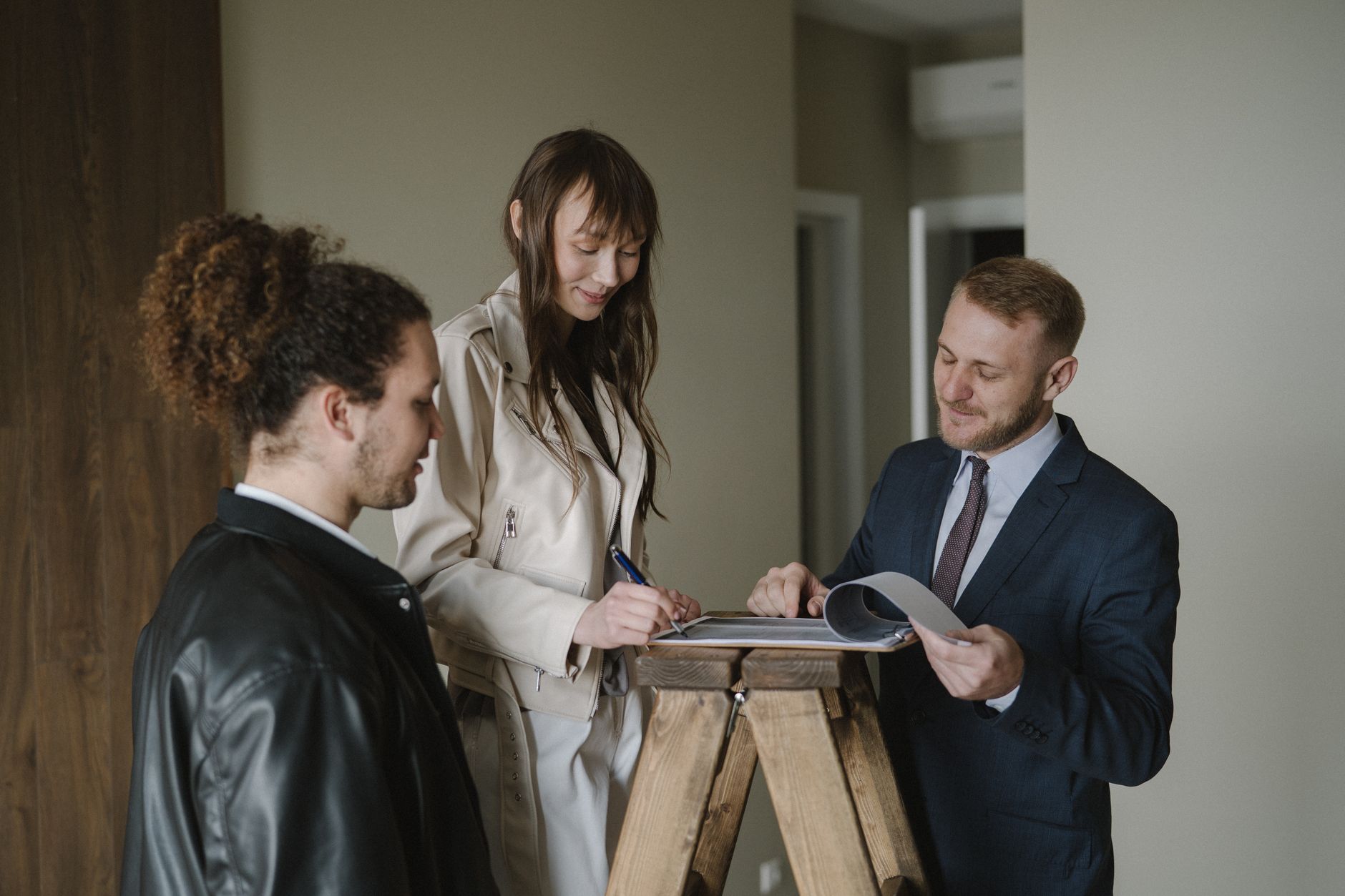 A couple signing real estate documents with an agent inside a new apartment.