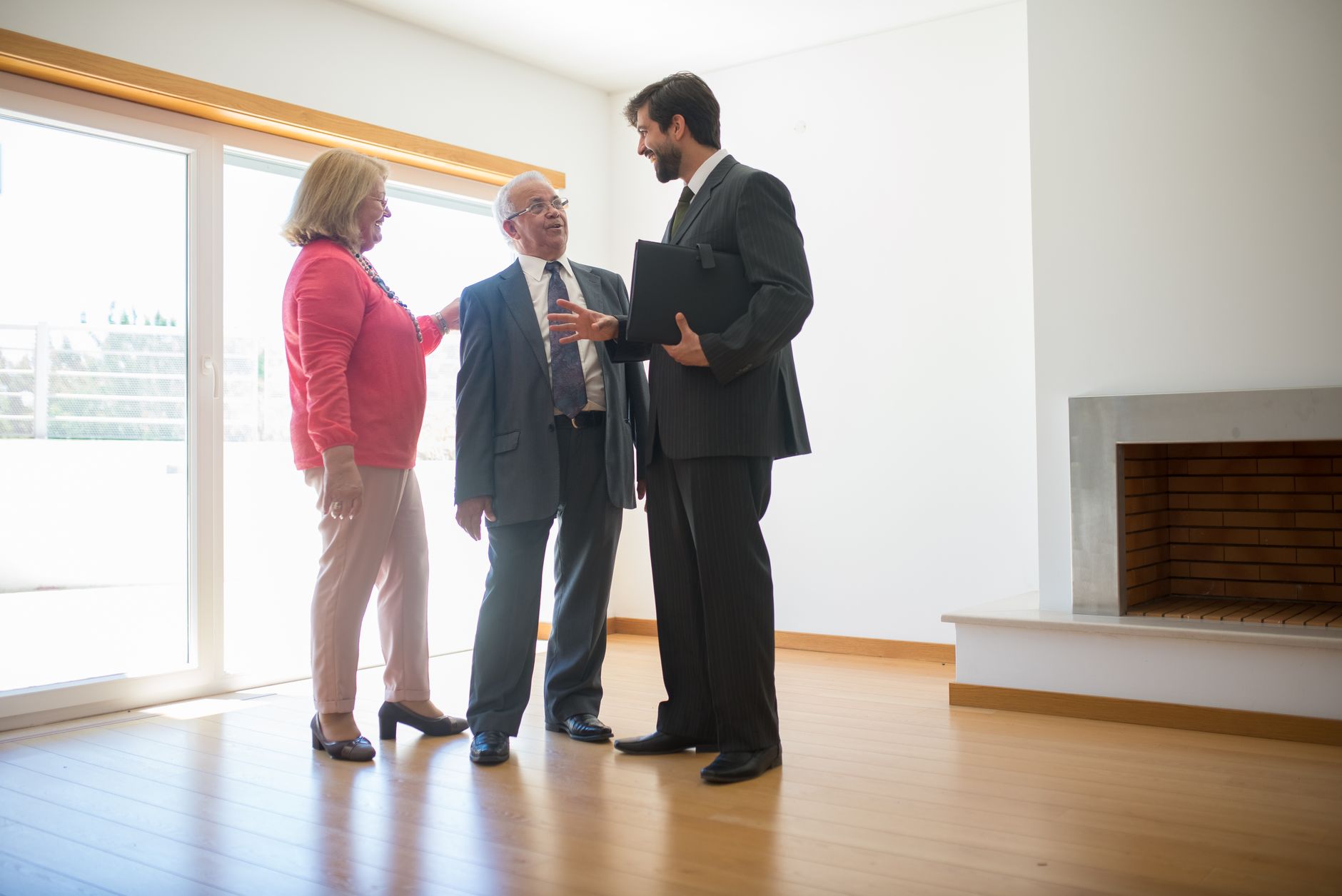 A real estate agent showing an empty house to two buyers in a bare living room