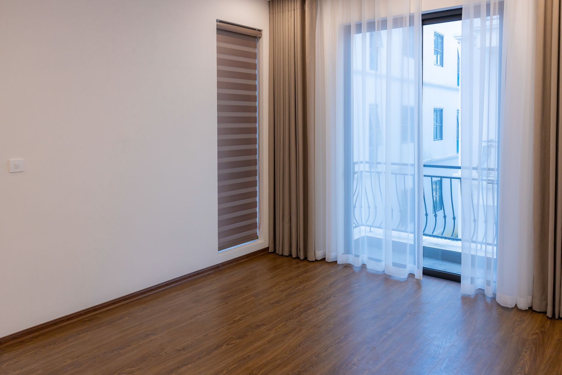 An empty apartment living room with a wooden floor and large windows, waiting for a tenant.