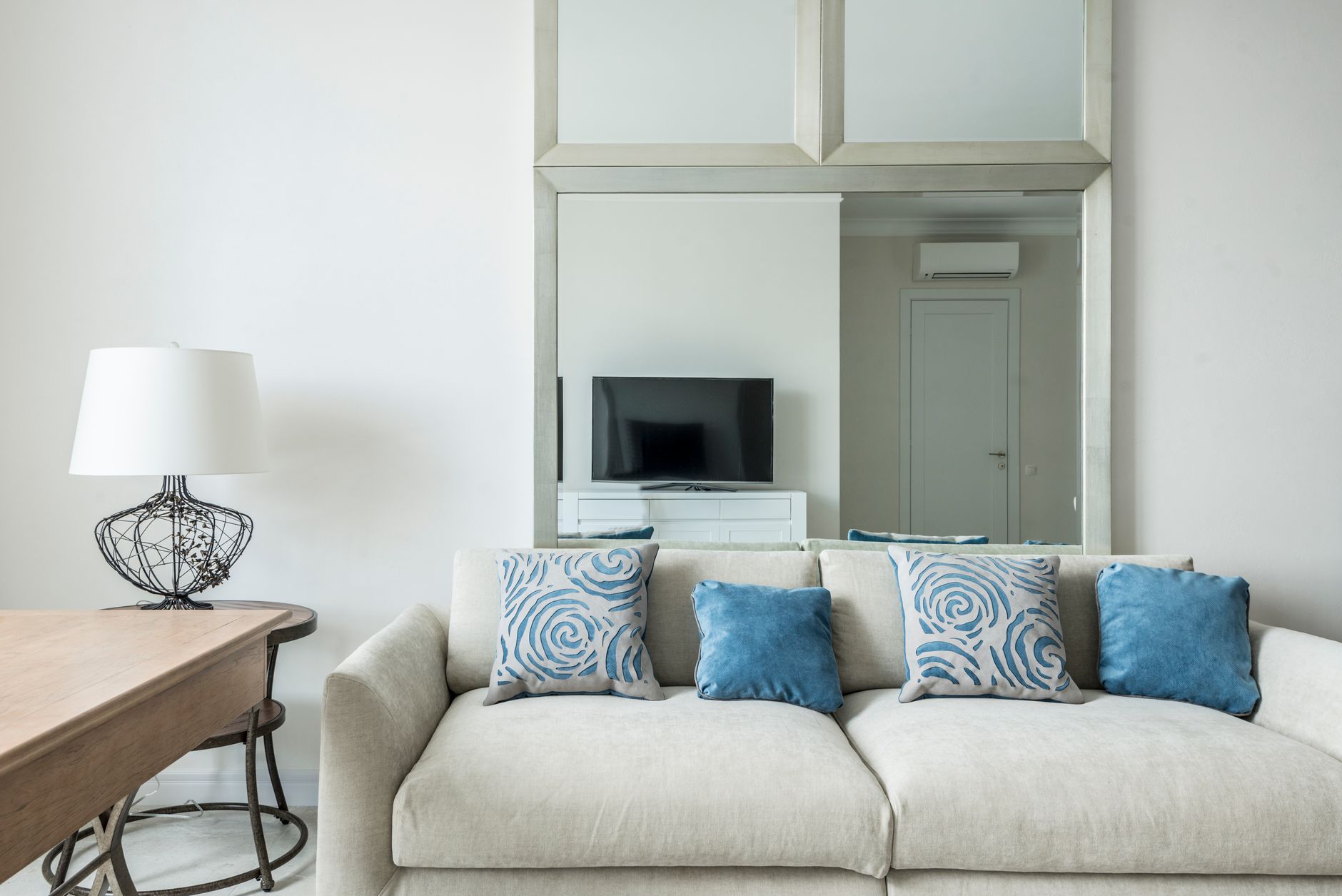A living room sofa with cushions arranged and a lamp on the side table, set up for a viewing