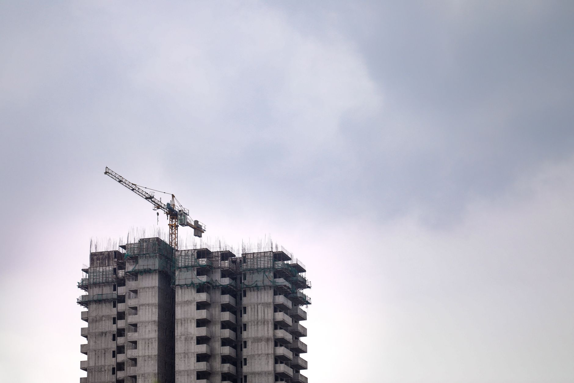 High rise condominium under construction with a tower crane against a cloudy sky