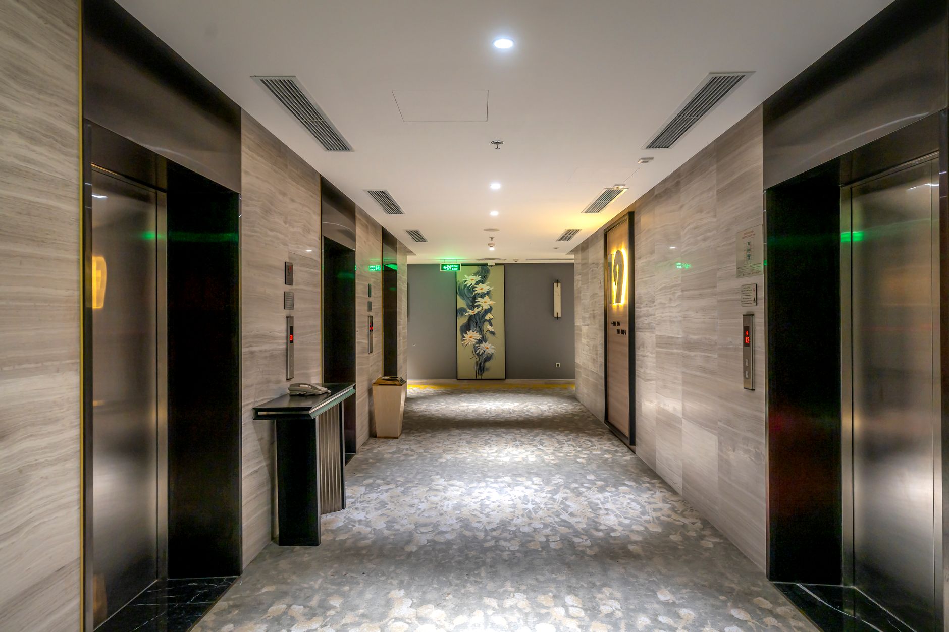 A long building corridor with elevator doors and a polished stone floor.