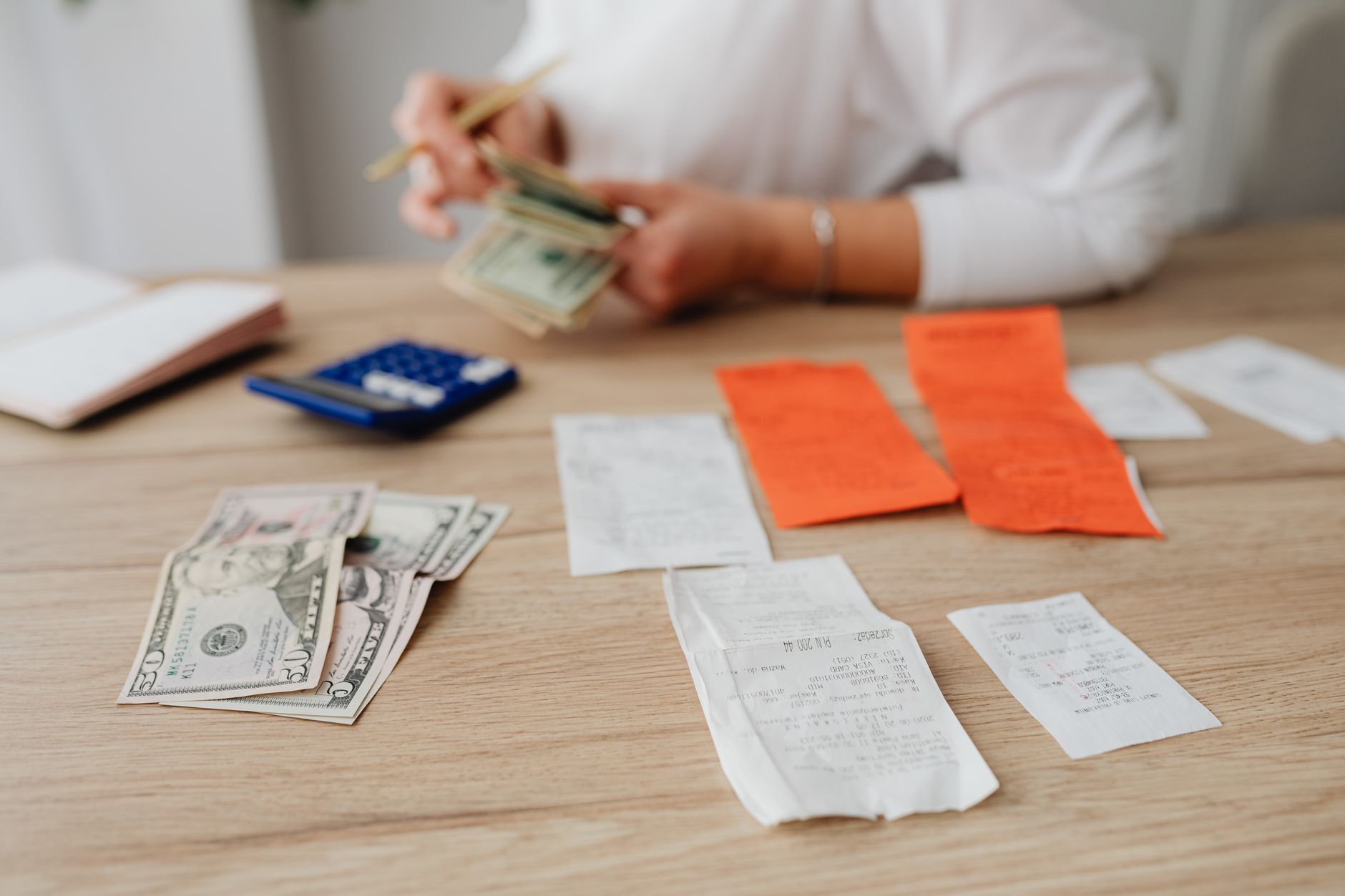 A person at a table with a calculator, cash and household bills.